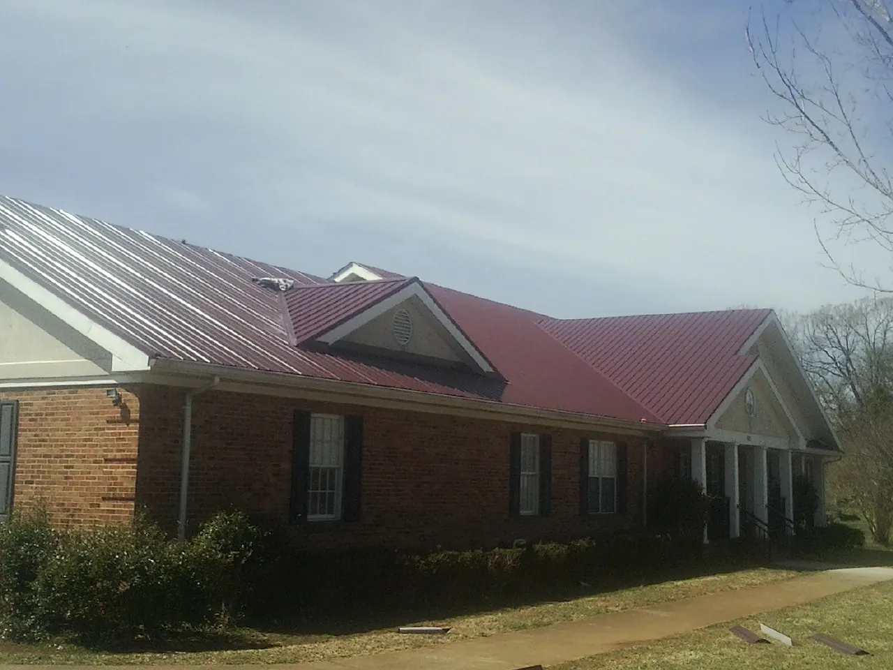 Red metal roof with gabled entries on a long brick building, from a Hail Damage Roof Repair job in Smiths Station