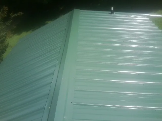 New green metal panels meeting at the ridge of a roof — Flat Roof Repair work by our crew in Smiths Station