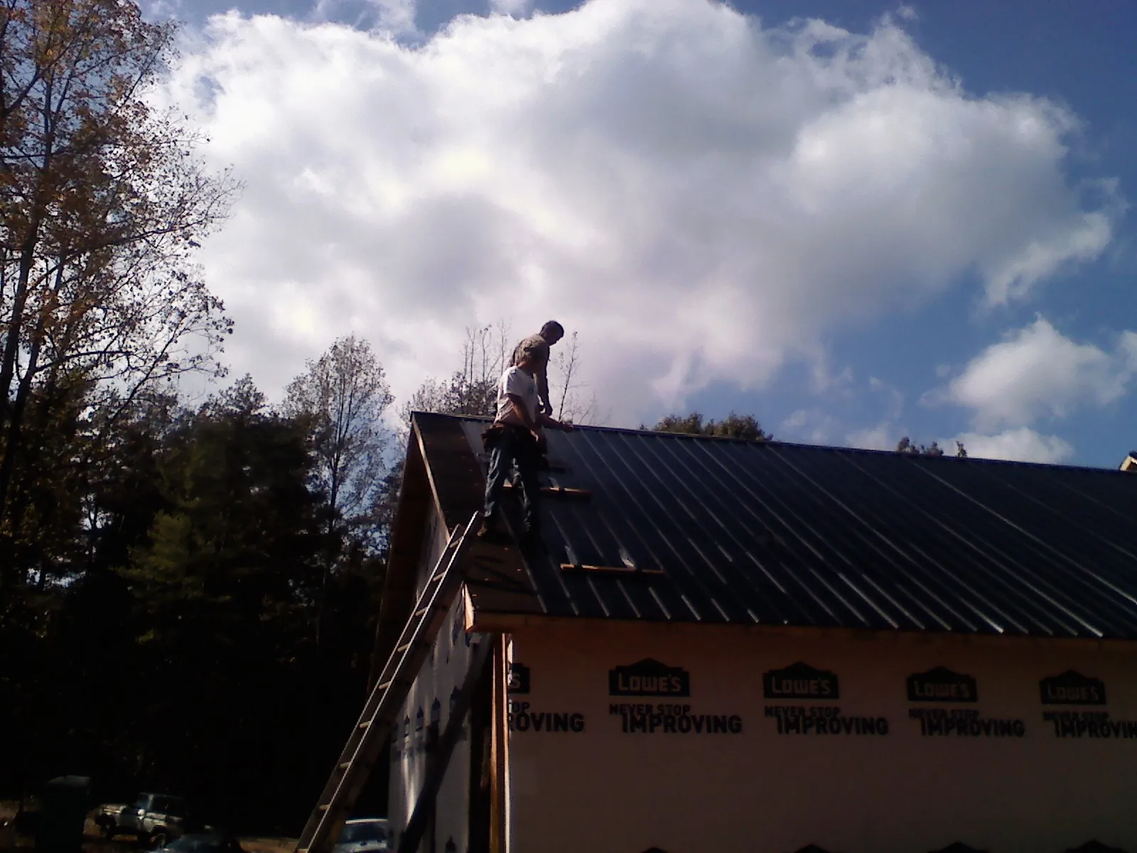 Roofer fastening dark metal panels high against a cloudy sky, from a Roof Inspection job in Smiths Station