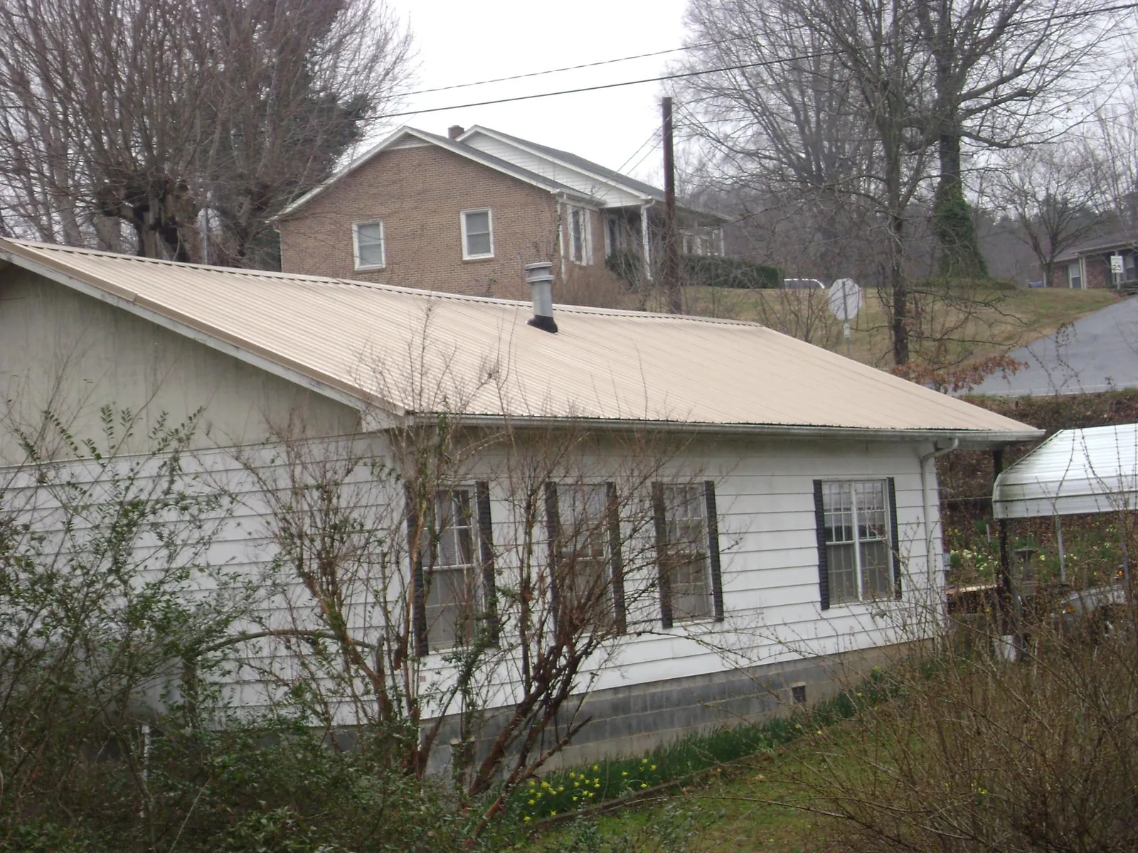 Tan metal roof on a white sided house set into a hillside — Commercial Roofing by Roofing Brothers in Smiths Station